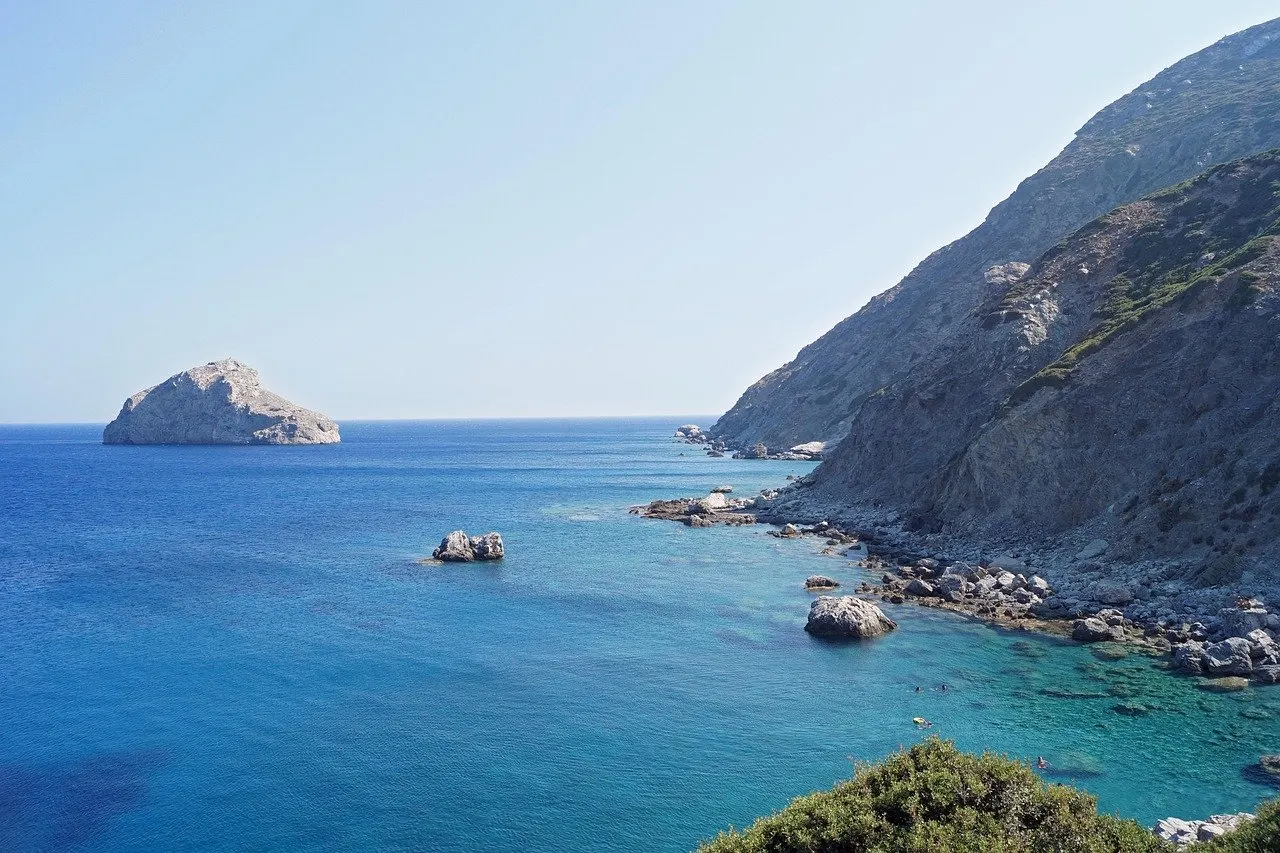 Steile, karge Felsküste auf Amorgos mit türkisblauem Wasser, einzelnen Felsbrocken in der Bucht und einer Felsinsel im Meer