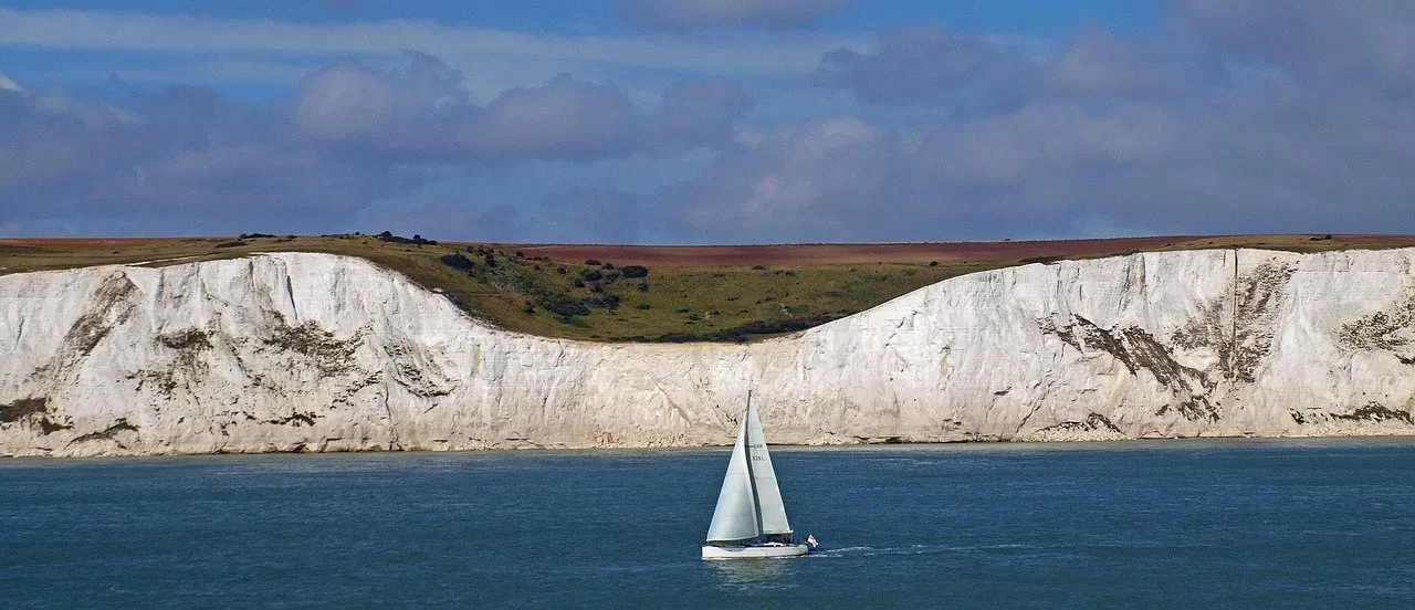 Weiße Kreidefelsen an der englischen Küste bei Dover, davor ein Segelboot auf dem blauen Ärmelkanal