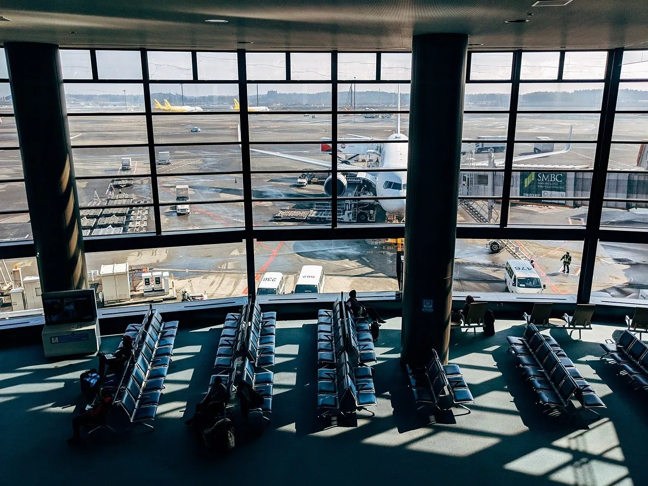 Wartebereich mit blauen Sitzreihen an einem japanischen Flughafen, durch die Glasfront sind ein Flugzeug am Gate und das Vorfeld zu sehen